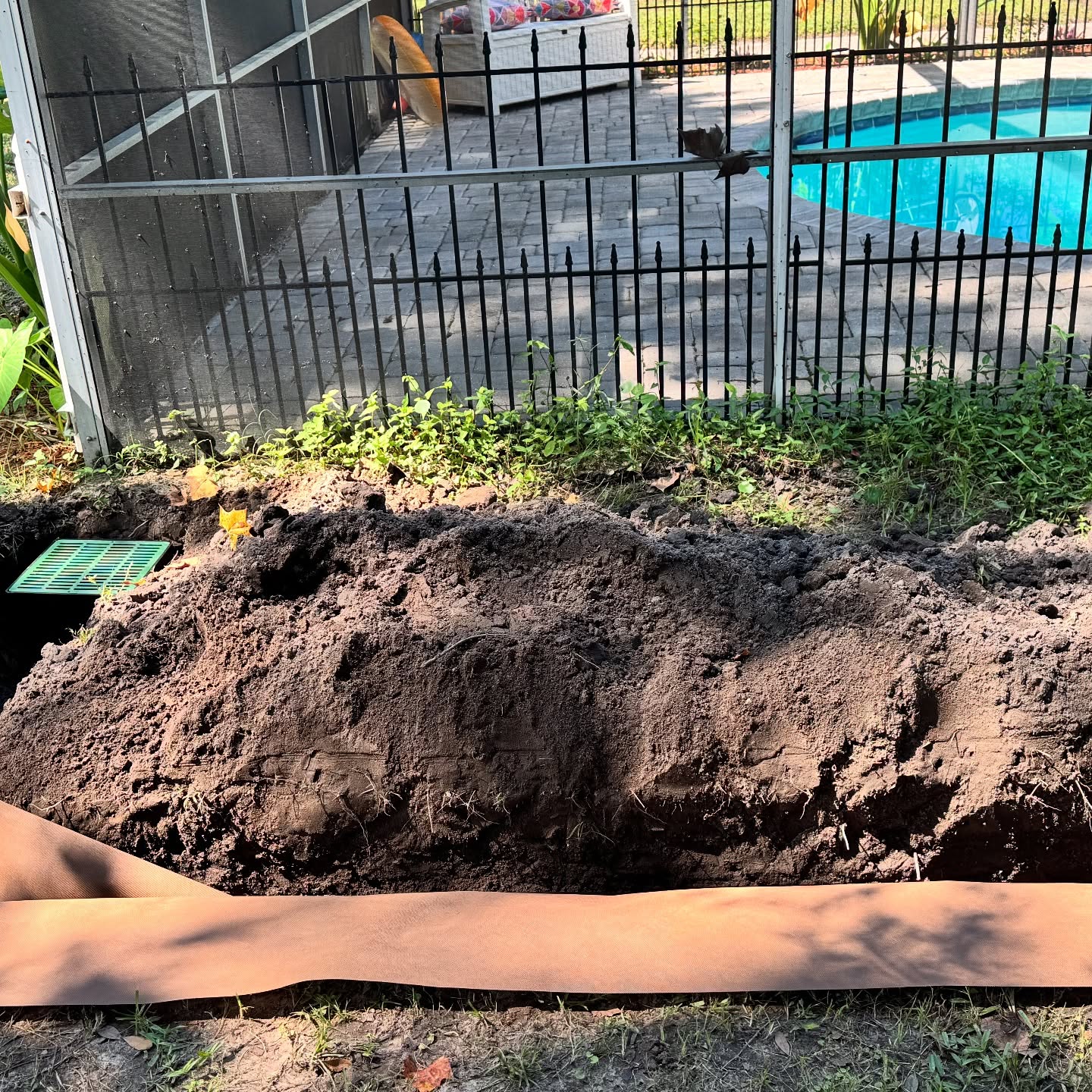 Drainage trench with green catch basin beside a pool fence